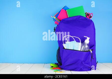 Backpack full of school supplies and COVID 19 prevention supplies. Blue background. Back to school during pandemic concept. Stock Photo