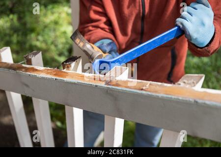 Man Using a Hammer and Pry Bar to Tear Down Old Deck Stock Photo