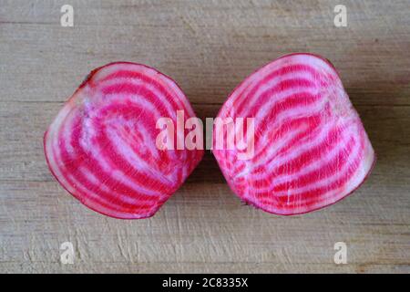 Colourful, cheerful, peppermint rings of red, pink and white hidden inside of a candy cane beet - sliced in two on a wooden chopping board. Stock Photo