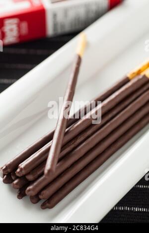 Vertical image of Pocky chocolate sticks place on a long white plate and box packaging in background. Stock Photo