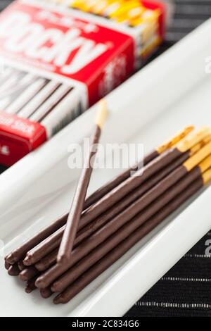 Vertical image of Pocky chocolate sticks place on a long white plate and box packaging. Stock Photo