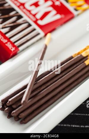 Vertical image of Pocky chocolate sticks place on a long white plate and box packaging. Stock Photo