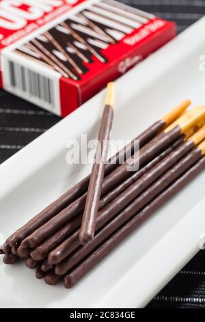 Vertical image of Pocky chocolate sticks place on a long white plate and box packaging. Stock Photo