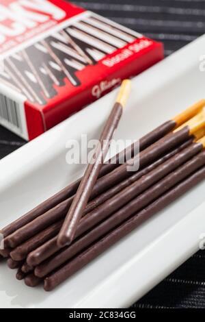 Vertical image of Pocky chocolate sticks place on a long white plate and box packaging. Stock Photo