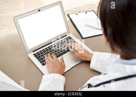Indian female doctor typing using laptop mock up white screen at desk, close up. Stock Photo