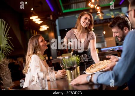 Pretty waiter woman serving group of friends with food in the restaurant Stock Photo