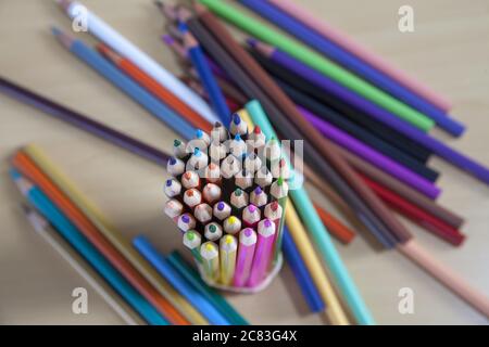 Selective focus shot of a bundle of colored pencils next to a few more on a wooden surface Stock Photo