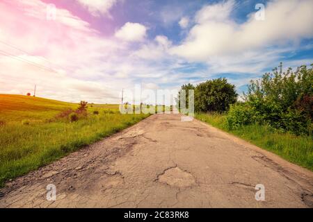 Old country road in potholes and holes. Rural landscape on a sunny day. Stock Photo