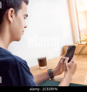 Young adult looking at mobile phone, sitting in cafe. Digital age. People communicate in chat. Stock Photo