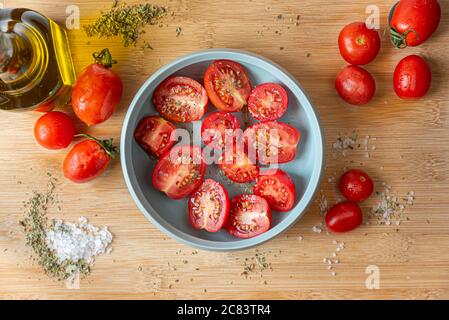 Naples, Italy. Food image of a bunch of tomatoes in a little turquoise bowl on a wooden cutting board with coarse salt, oregano and a glass oil cruet Stock Photo