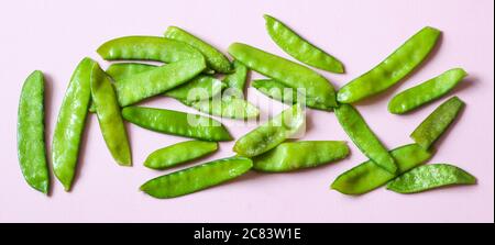 Frozen vegetables such as pea pods spread out on the button edge on a pink background. Top view. Banner. Horizontal orientation Stock Photo