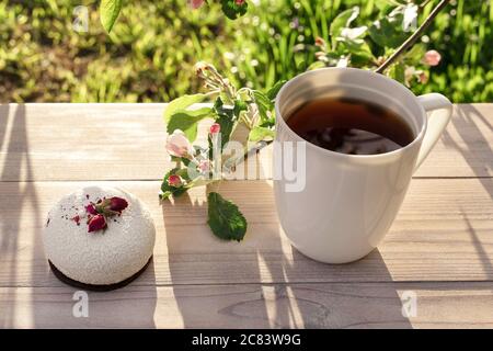 Beautiful porcelain coffee cup with mousse pastry dessert decorated with pink apple tree branches in bloom on wooden table. Spring garden in setting s Stock Photo