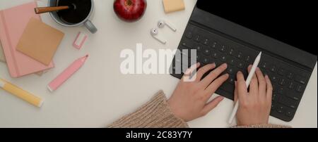 Overhead shot of female hands typing on tablet keyboard while holding stylus pen on white worktable with stationery Stock Photo