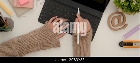 Overhead shot of female student hands using digital tablet with keyboard and stylus pen on white table with stationery Stock Photo