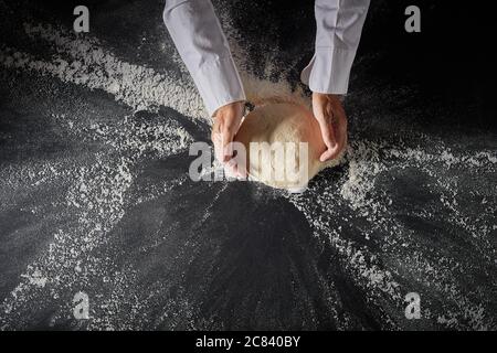 Baker or chef in an Italian pizzeria kneading a mound of dough on a floured slate surface viewed top down on his hands with copyspace Stock Photo