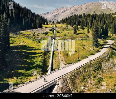 Man on mountain bike rides on the road to the mountain valley against blue cloudy sky. Recreation and healthy lifestyle concept Stock Photo