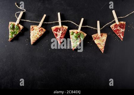 Pizza portions with an assortment of trimmings hanging from a string border by clothes pegs over copyspace below for menu advertising Stock Photo