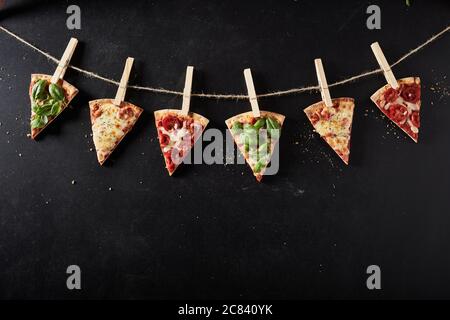 Tasty assortment of Italian pizza toppings on sliced freshly baked pizza portions pegged to a string over a slate background with copyspace for menu a Stock Photo