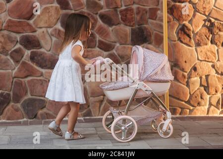 Little girl in white dress rolls the stroller by the home Stock Photo