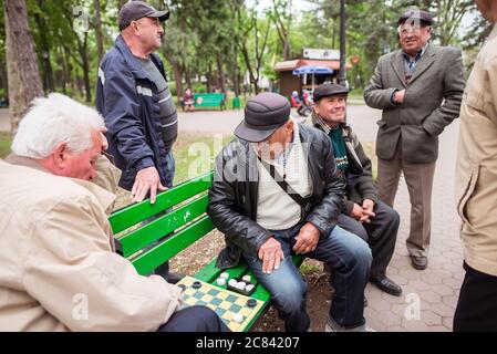 Chisinau / Moldova - May 15, 2020: group of adult men playing chess on green bench in large park of the capital of Moldova Stock Photo