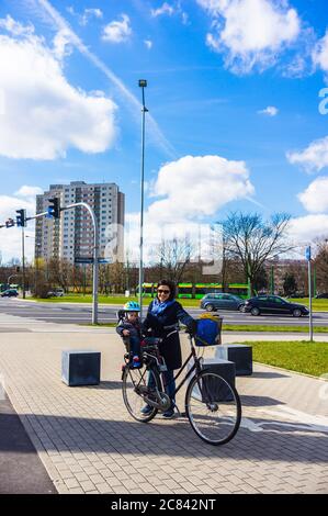 POZNAN, POLAND - Mar 21, 2019: Woman standing by a bicycle with child sitting in a seat on a sidewalk at the Rataje district Stock Photo