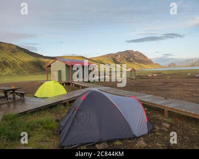 Colorful tents at camping site on blue Alftavatn lake with green hills and glacier in the otherwordly beautiful landscape of the Fjallabak Nature Stock Photo