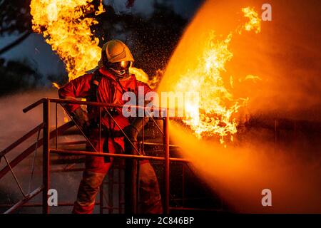 Firefighter using water fog type fire extinguisher to fighting with the fire flame from oil pipeline leak and explosion on oil rig and natural gas sta Stock Photo