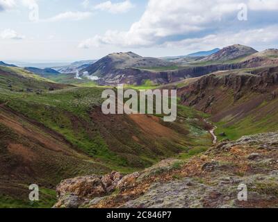 Reykjadalur valley with hot springs river with lush green grass meadow and hills with geothermal steam. South Iceland near Hveragerdi city. Summer Stock Photo
