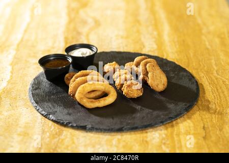 Closeup shot of chicken nuggets on a black round board on a wooden table Stock Photo