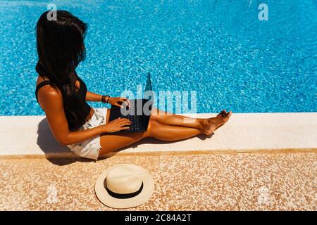 Woman digital nomad working in the swimming pool with laptop. Wireless workplace Stock Photo