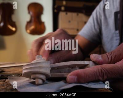 Hands of luthier violin maker carving and working on a instrument scroll  in his workshop in Cremona, Italy Stock Photo