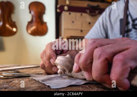 Hands of luthier violin maker carving and working on a instrument scroll  in his workshop in Cremona, Italy Stock Photo