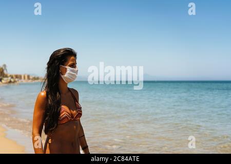 Young woman in the beach wearing a face mask protection against covid or covid19 Stock Photo