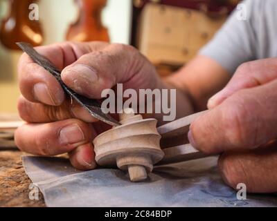 Hands of luthier violin maker carving and working on a instrument scroll  in his workshop in Cremona, Italy Stock Photo