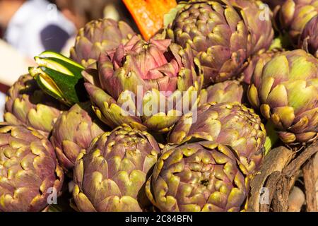 Fresh big Romanesco artichokes, green purple flower heads on a market place. Stock Photo