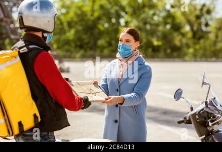 Courier Delivering Package To Customer Girl Standing Outdoors, Wearing Masks Stock Photo