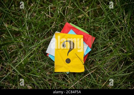 Pile of colorful paper notes with question marks on green grass. Close up. Stock Photo