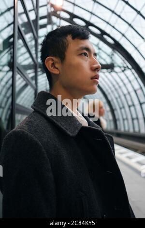 Side view of young Asian businessman thoughtfully waiting train at station Stock Photo