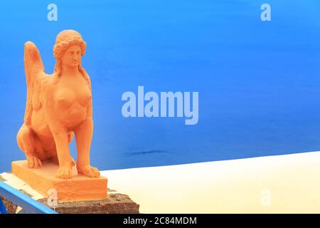 Sphinx orange statue, woman with the body of a lion with wings, mythology animal in Greece, Santorini, Oia and blue sea copy space background Stock Photo