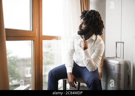 Black man businessman sitting and looking at window in hotel room Stock Photo