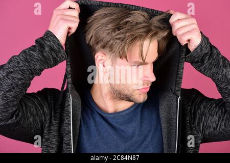 Macho with concentrated face takes hood on. Sports fashion and confidence concept. Man with fair hair on purple background. Guy with bristle in dark blue tshirt and grey hoodie Stock Photo