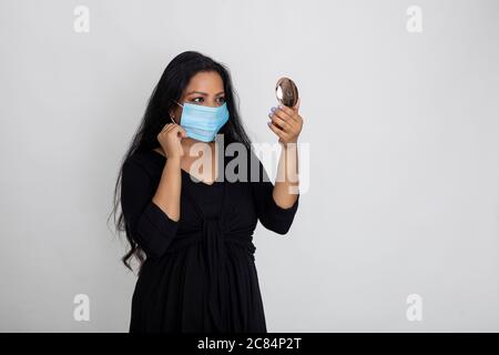 Indian woman wearing Covid protection mask, Lady looking at herself in a hand mirror Stock Photo
