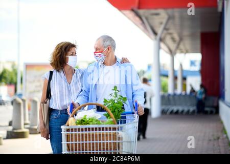 Senior couple with face masks and shopping walking outside supermarket in city. Stock Photo