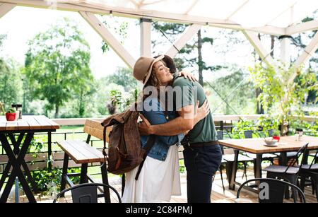 Happy couple greeting outdoors on terrace restaurant, hugging. Stock Photo
