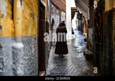 Morocco, Tangier: Scene from everyday life with inhabitants in the medina. Elderly man in striped bournous viewed from behind walking alone in a cobbl Stock Photo