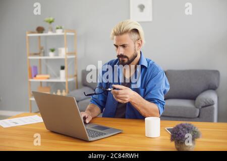 Serious young man working on laptop from home. Student taking online educational course or communicating with teacher Stock Photo