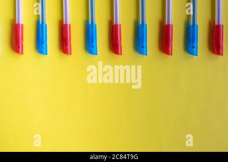 Mixed blue and red ballpoint pens on a yellow background from above. Flat lay, top view, place for text. Stock Photo