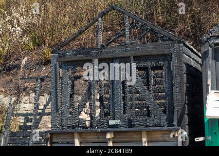 Bournemouth, Dorset UK. 21st July 2020. Aftermath of fire at West Cliff beach, Bournemouth which started in beach hut, showing remains of skeletal charred remains of beach hut with damage to neighbouring ones and charred remains of cliffside behind.  Credit: Carolyn Jenkins/Alamy Live News Stock Photo