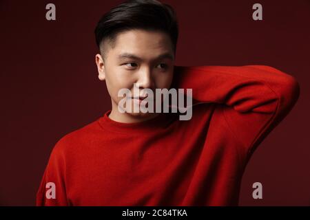 Image of calm young asian man posing and looking aside isolated over burgundy background Stock Photo