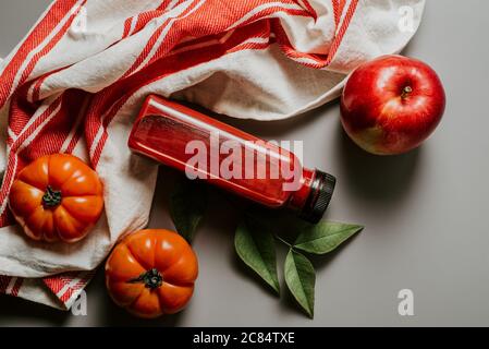 Red smoothie drink in bottle surrounded by red apples, tomatoes and beets on striped kitchen rag. Detox diet for healthy body and mind. health food co Stock Photo
